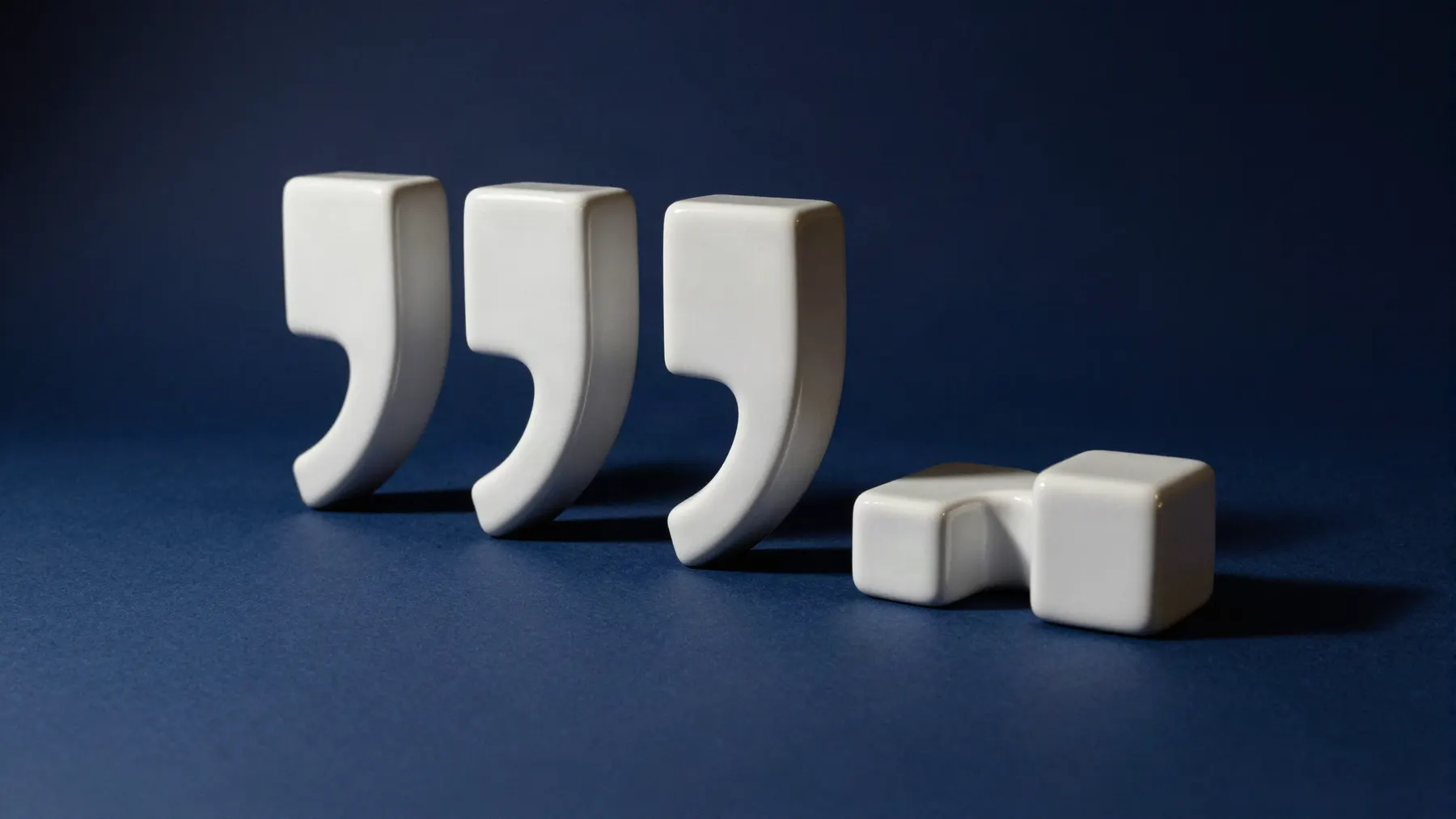 Four white ceramic comma sculptures standing in a row on a navy backdrop, the fourth toppled over.
